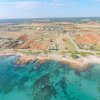 Costa rocciosa con mare azzurro e terreni agricoli.