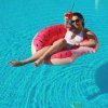 Persona in piscina su ciambella gonfiabile con drink arancione.