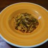 Piatto di pasta condita in un piatto arancione su tavolo di legno.