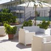 Terrazza con sedie bianche, tavoli e vegetazione, palazzo bianco sullo sfondo.