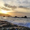 Spiaggia con onde al tramonto e montagne sullo sfondo.