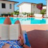 Persona legge a bordo piscina con case sullo sfondo.