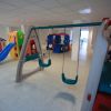 Interno di un'area giochi con altalene e scivolo.