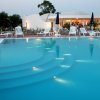 Piscina con gradini illuminati di sera, lettini bianchi e ombrelloni blu.