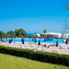 Piscina con ombrelloni blu, veduta di alberi e mare sullo sfondo.