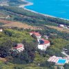 Vista aerea di un complesso turistico con piscine, immerso nel verde vicino alla costa.