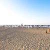 Spiaggia sabbiosa con ombrelloni blu e persone che camminano sul bagnasciuga.