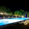 Piscina illuminata di notte con sdraio e ombrelloni blu, circondata da alberi.