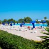 Piscina azzurra con lettini e ombrelloni blu, circondata da siepi e alberi.