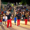 Un gruppo di persone balla davanti a un pubblico in un anfiteatro all'aperto, di sera.