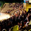 Un ampio pubblico osserva uno spettacolo serale in un anfiteatro all'aperto.