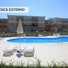 Piscina con lettini e ombrelloni, edificio residenziale sullo sfondo.