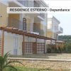 Edificio con balconi, pergolato in legno, siepi e vialetto di accesso.
