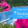 Una piscina con fiori rosa in primo piano e un cartello che promuove un campeggio.