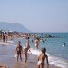 Spiaggia affollata con persone che camminano e giocano vicino all'acqua.