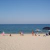 Spiaggia sabbiosa con persone in lontananza e ombrelloni neri e a righe.