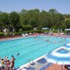 Piscina all'aperto con nuotatori e ombrelloni blu.