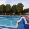 Una piscina vuota con scivolo, lettini e ombrelloni, circondata da alberi.