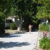 Una strada in un campeggio con case mobili e alberi. Una persona cammina su un viale soleggiato.