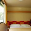 Stanza con letto matrimoniale, pareti beige e finestra con tende gialle.
