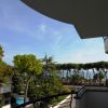 Balcone con vista su alberi, piscina e mare in lontananza.