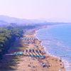 Lunga spiaggia affollata con mare a sinistra.