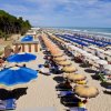 Spiaggia affollata con file di ombrelloni colorati.