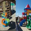 Parco giochi sulla sabbia con dondolo colorato e scivolo a torre multicolore.