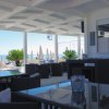Una terrazza coperta vista mare con tavoli e sedie, circondata da piante e ombrelloni.