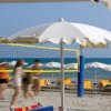 Persone che giocano a pallavolo su una spiaggia con ombrelloni bianchi e sedie a sdraio.