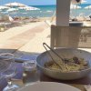 Piatto di spaghetti alle vongole su tavolo affacciato su spiaggia con ombrelloni e mare.