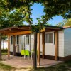 Bungalow con portico e sedie verdi tra gli alberi.