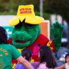 Mascotte verde con cappello giallo e bambini intorno.