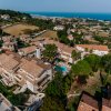 Complesso residenziale con piscina, colline e mare sullo sfondo, vista aerea.