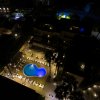 Piscina illuminata di notte vista dall'alto, circondata da edifici.