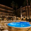 Piscina a forma libera illuminata di notte con lettini e palme, davanti a un edificio.