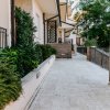 Entrata di una casa con marciapiede piastrellato, fioriere e ringhiera metallica.