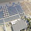 Spiaggia con file ordinate di ombrelloni blu e arancioni visti dall'alto.