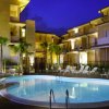 Piscina illuminata di notte, circondata da lettini e edifici residenziali.
