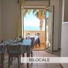 Sala con tavolo e sedie, vista su balcone e mare.
