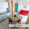 Cucina e soggiorno con divano rosso e tavolo da pranzo in un trilocale.