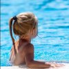 Bambina di spalle in piscina, con capelli biondi legati.