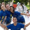 Quattro persone sorridenti partecipano a una festa in schiuma all'aperto, indossando magliette blu.