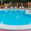 Piscina azzurra circondata da lettini bianchi e palme, con pavimento in legno chiaro.