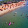 Spiaggia affollata con ombrelloni arancioni e persone in acqua.