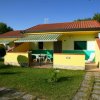 Un bungalow giallo con tetto rosso, giardino e veranda con tavolo.