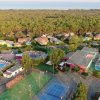 Vista aerea di una struttura turistica con piscina, campi sportivi e case tra gli alberi.