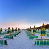 Spiaggia con lettini e ombrelloni gialli e verdi sotto un cielo al tramonto.