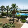 Piscina all'aperto con lettini, palme e vista sul mare.