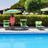 Una piscina blu con sdraio e ombrellone giallo-verde, persona di spalle in vestaglia rosa.